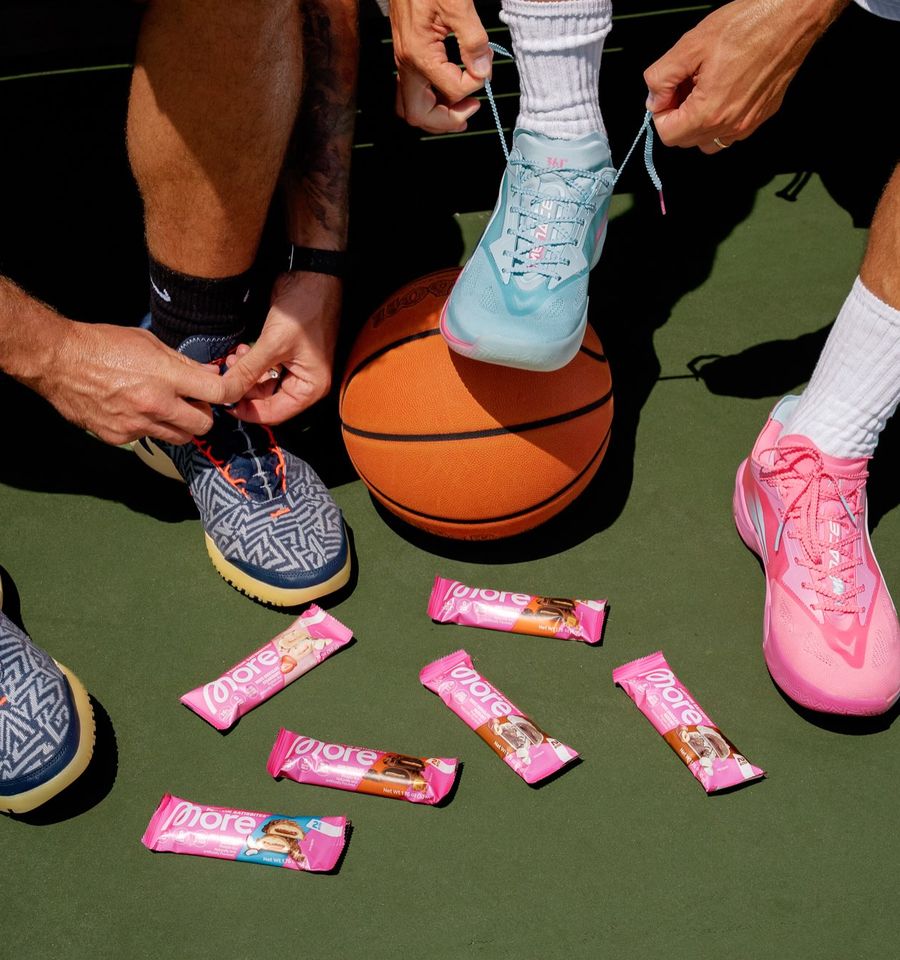 Two players lacing up basketball shoes over a ball, More packs scattered on the court.